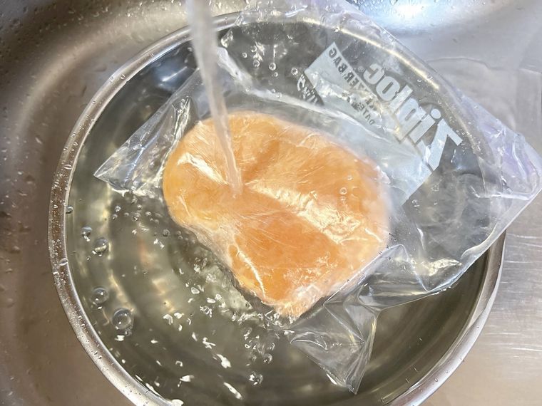 フリーザーバッグに入った冷凍肉を流水で解凍する様子