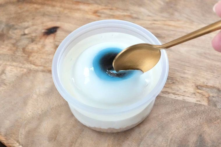 木のカッティングボードにのった目玉のレアチーズケーキを金のスプーンで食べる様子