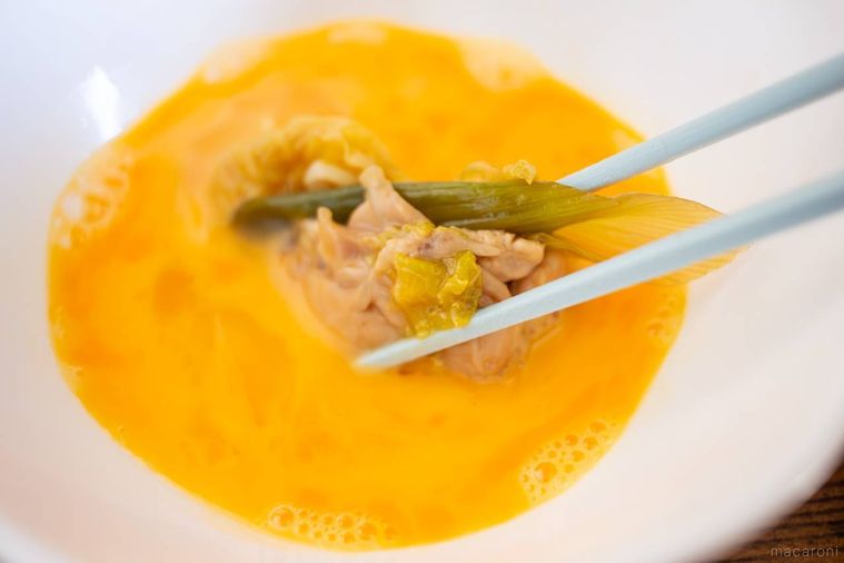 取もも肉と長ねぎを箸で溶き卵に浸している様子