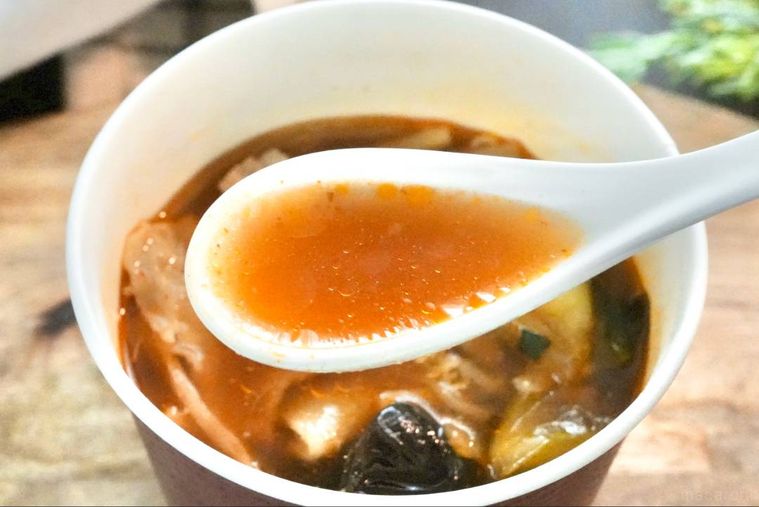 木のカッティングボードにのったコンビニの麻辣湯カップスープを白いれんげですくう様子