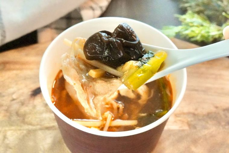 木のカッティングボードにのったコンビニの麻辣湯カップスープの具材を白いれんげですくう様子