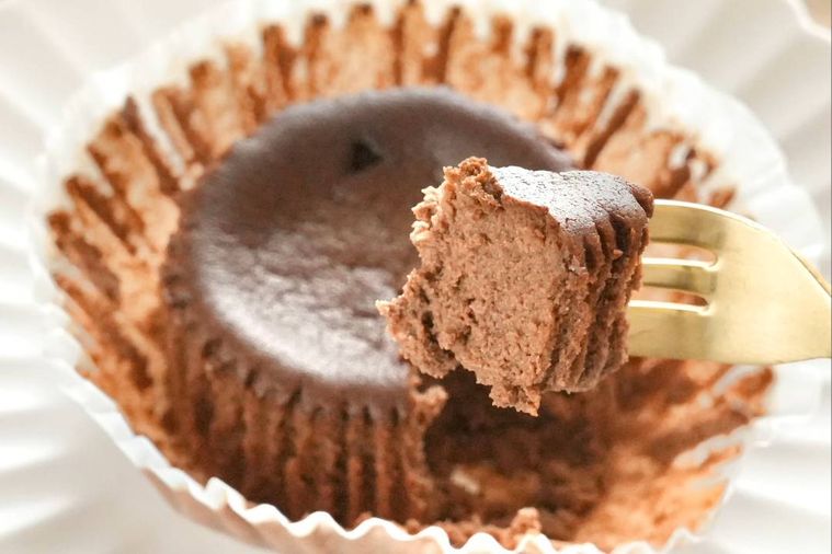 木のカッティングボードと白い皿にのったショコラベイクドチーズケーキを金のフォークで食べる様子