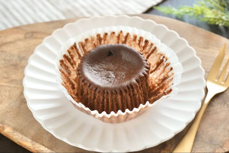 木のカッティングボードと白い皿にのったショコラベイクドチーズケーキと金色のフォーク