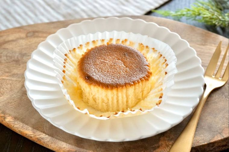 木のカッティングボードと白い皿にのったベイクドチーズケーキと金のフォーク