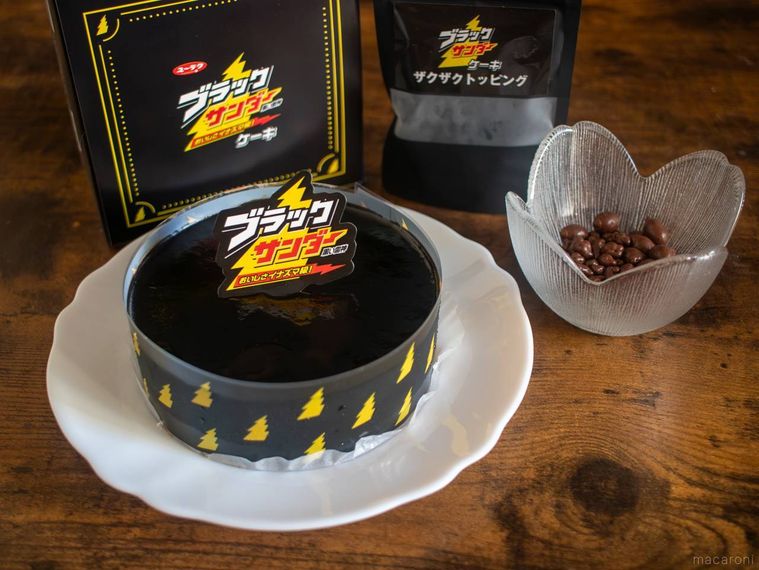 お皿にのせたブラックサンダーケーキとザクザクトッピングを外装とともに木製のテーブルに並べている