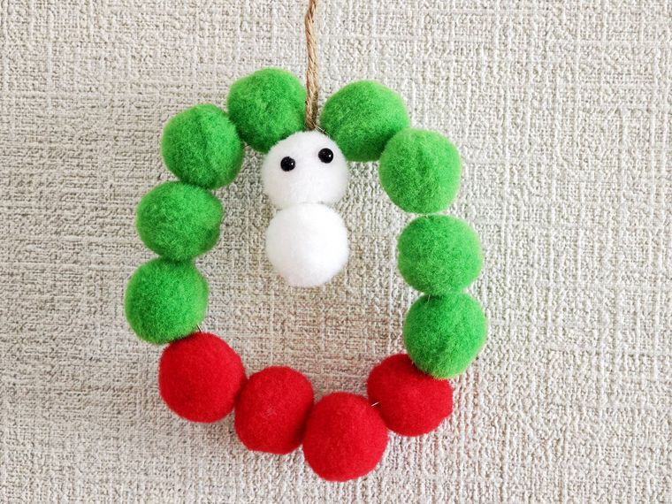 ポンポンで作る雪だるま付きのリースを壁に飾っている状態