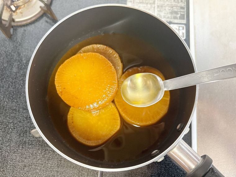 鍋に入った大根の煮物に酢を加える様子
