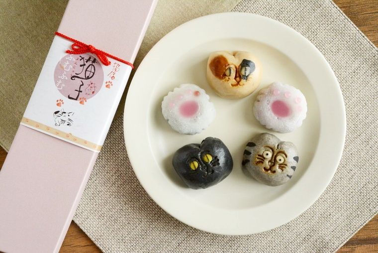 お皿に並べられた三毛猫や黒猫などの形をした招福猫子まんじゅうふむふむとパッケージが並んでいる様子