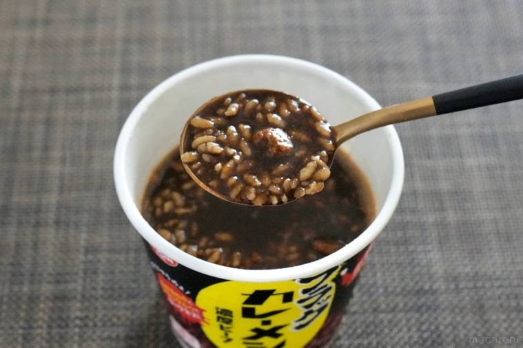 黒いカップのカレーメシを金色のスプーンで食べる様子