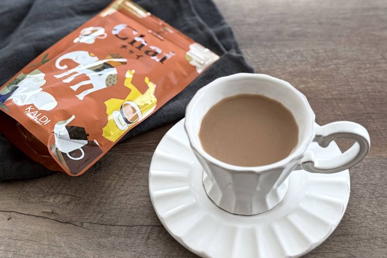 木のテーブルの上にマサラチャイが入った白いカップとインスタントチャイのパッケージが置かれている