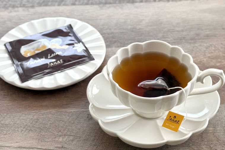 木のテーブルの上に紅茶が注がれた白いカップとパッケージが乗った白いお皿が置かれている