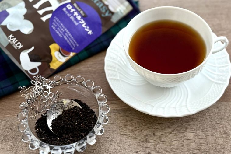 木のテーブルの上にロイヤルブレンドと紅茶が注がれた白いティーカップと茶葉が入ったガラスのココットが置かれている