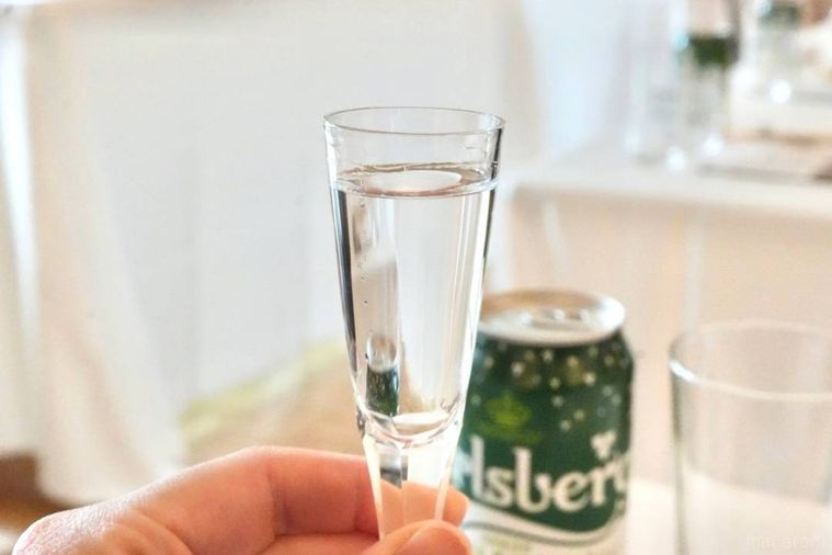 グラスに入ったアクアビットを持つ手とチェイサーのグリーンの缶