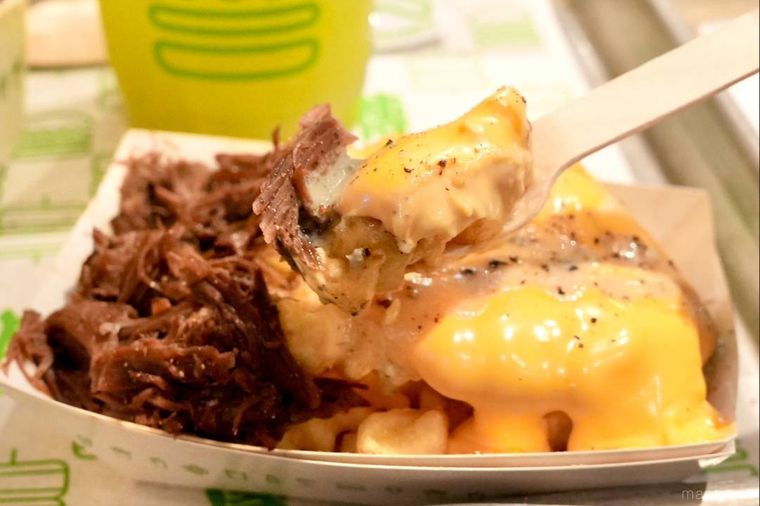 紙トレーにのった牛頬肉の煮込みとチーズがトッピングされたフライドポテトメニューをフォークで食べる様子