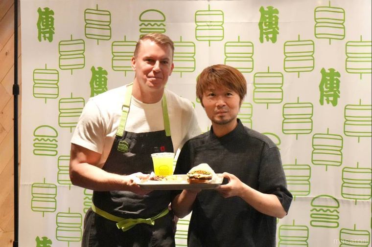 ディレクターとシェフが限定のコラボハンバーガーとドリンクを持つ様子