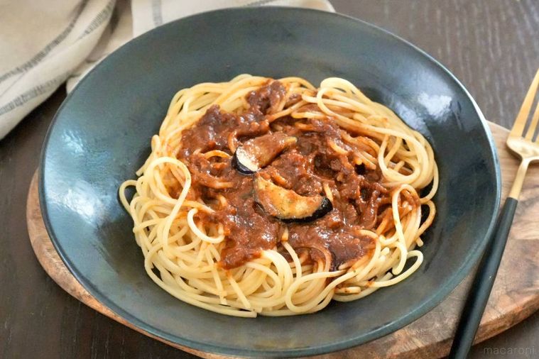 木のカッティングボードと黒い皿にのった冷凍ボロネーゼと黒と金のフォーク