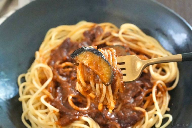 黒い皿にのった冷凍ボロネーゼを黒と金のフォークで食べる様子