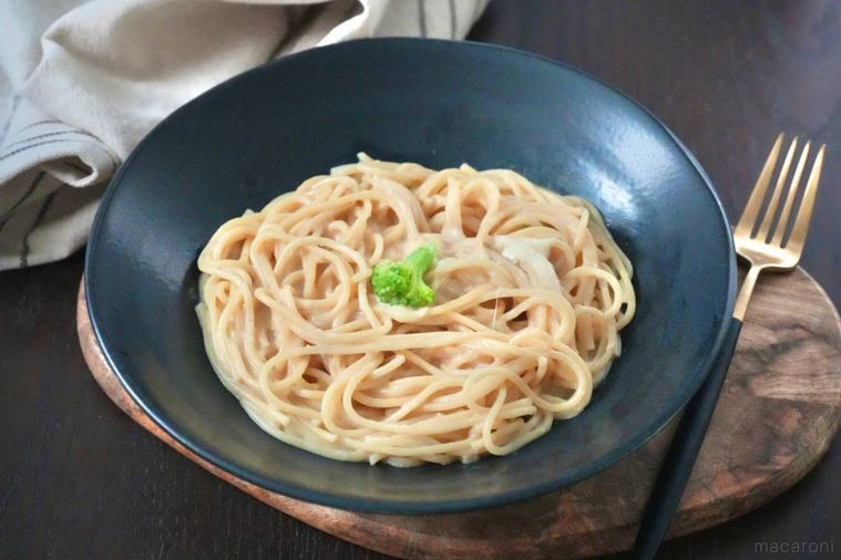 木のカッティングボードと黒い皿にのったシュクメルリ風のパスタと金色と黒色のフォーク