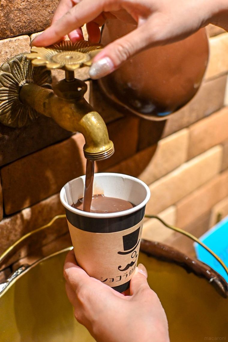 蛇口から出ているチョコレートのドリンクをカップに注いでいるところ