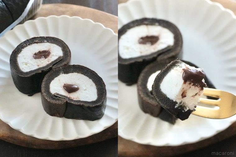 木のカッティングボードと白い皿にのった黒いロールケーキと金のフォークで食べる様子