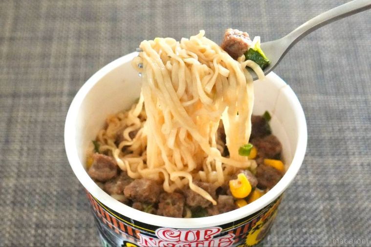 ガーリックペッパー味のカップヌードルの麺と具材を銀色のフォークで持ち上げて食べる様子