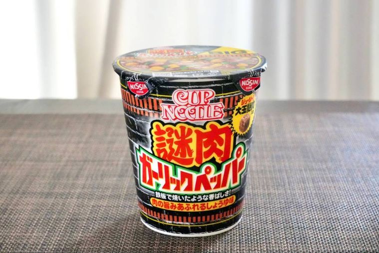 茶色いランチョンマットにのった黒いパッケージの謎肉ガーリックペッパーカップヌードル