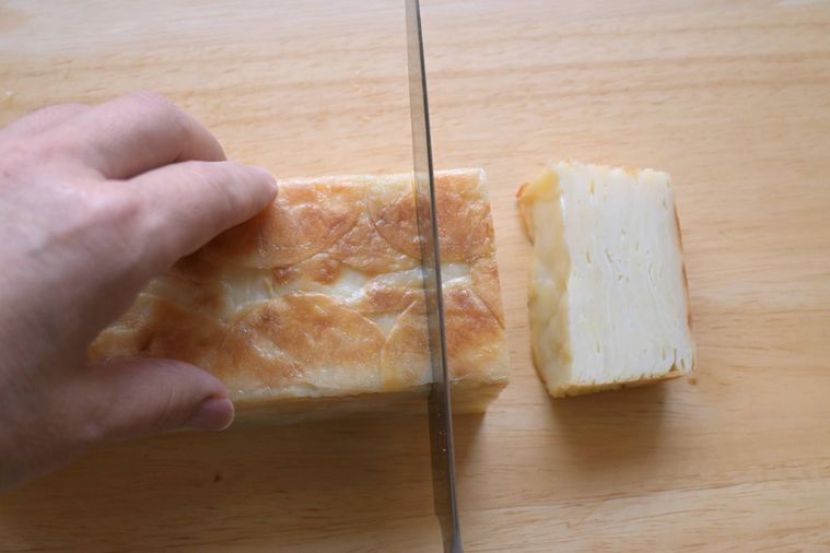 型から出したじゃがいもの重ね焼きを包丁でカットする様子