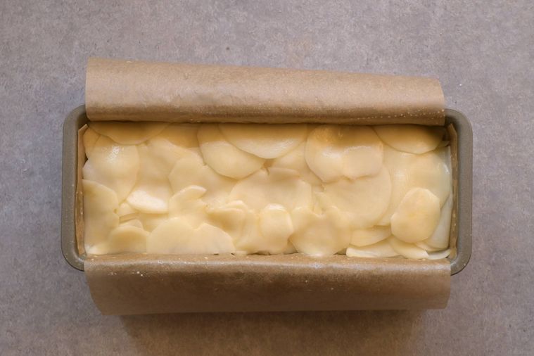 クッキングシートを敷いたパウンド型に薄切りじゃがいもが重ねられている