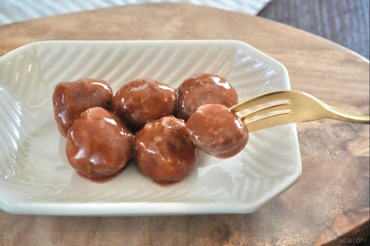 木のカッティングボードと白い皿にのったミートボールを金色のフォークに刺した様子