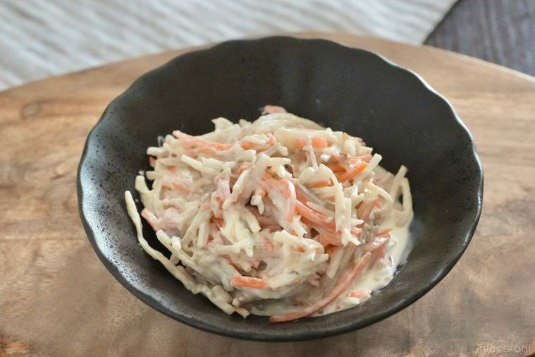 木のカッティングボードにのった黒い器に盛られたごぼうサラダ