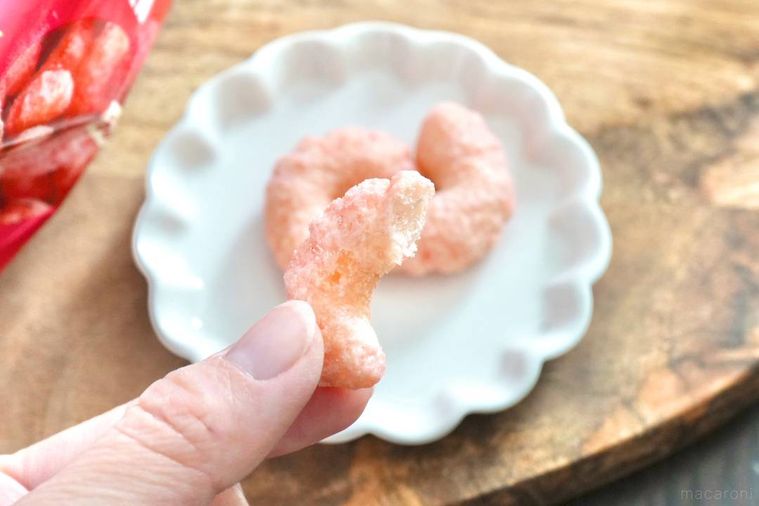 木のカッティングボードと白い小皿にのったあまおう苺味のキャラメルコーンを手に持つ様子