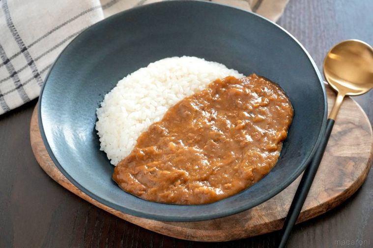 木のカッティングボードにのった黒い器に盛られたキーマカレーと黒色と金色のスプーン