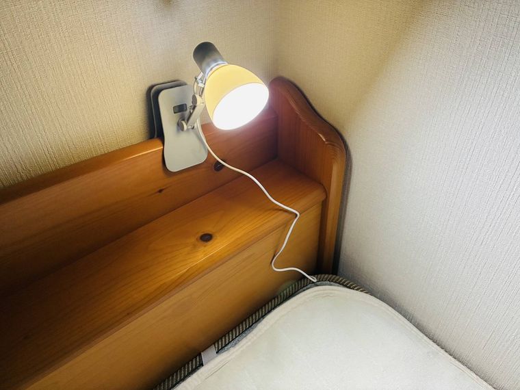 ベッドのヘッドボードに挟んでいる電気がついたクリップライト