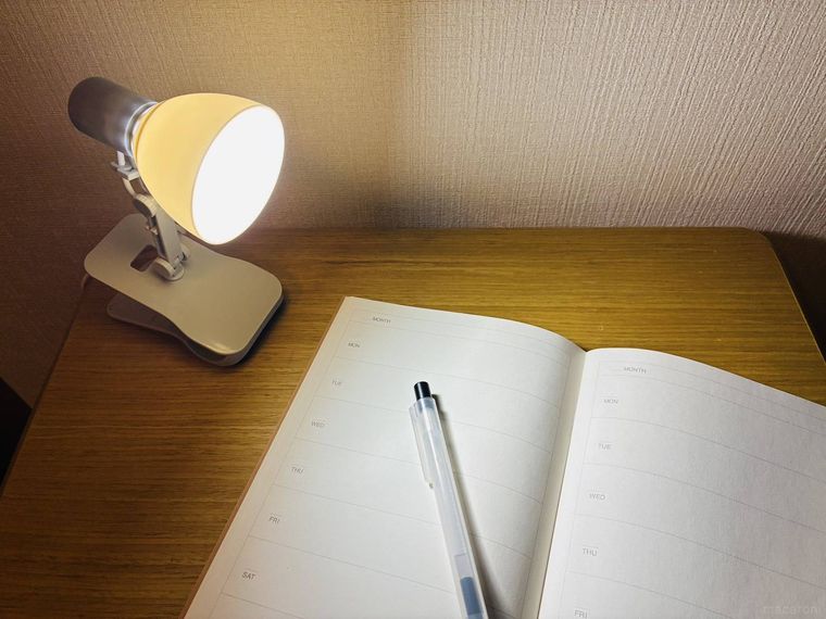 テーブルの上にある電気がついたクリップライトと手帳とペン
