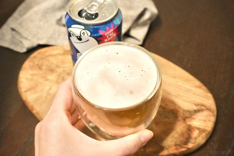 木のカッティングボードにのった青い缶のクラフトビールとグラスを手に持つ様子