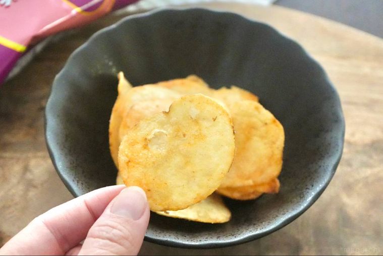 木のカッティングボードと黒い皿にのったポテトチップスを持つ手