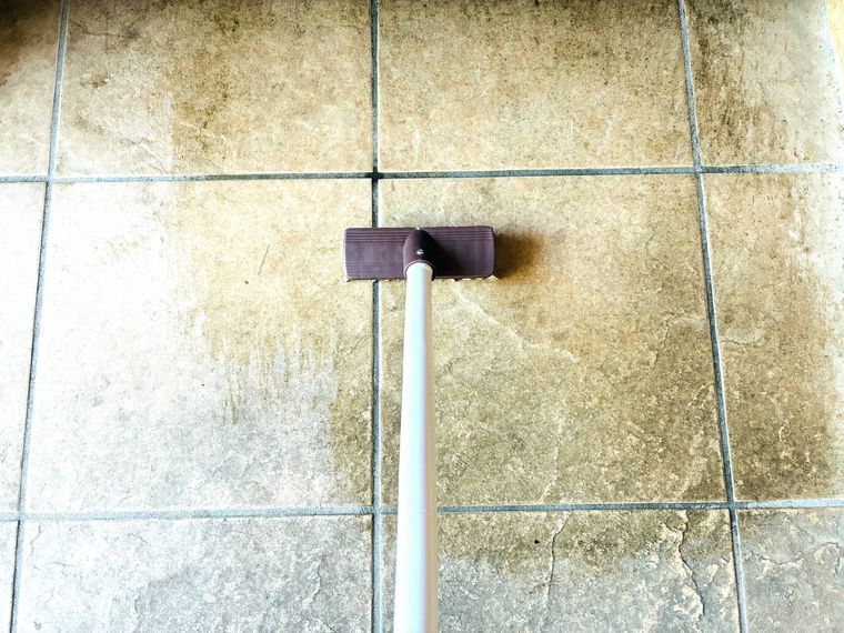 土間のタイルをデッキブラシでこすっている