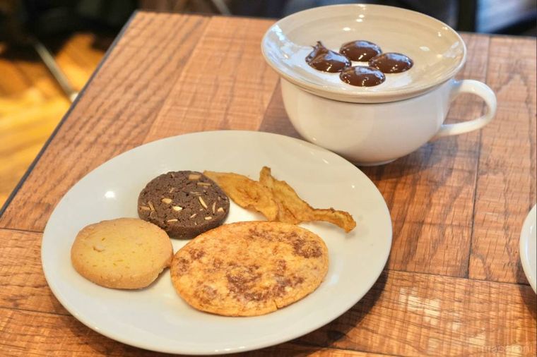 白い器に盛られた煎餅・サブレ・ごぼうチップスやチョコレートとティーカップ
