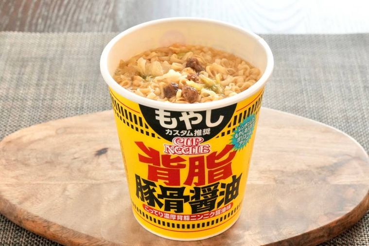 木のカッティングボードにのった黄色いパッケージの豚骨醤油カップヌードル