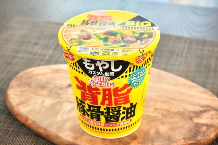 木のカッティングボードにのった黄色いパッケージの豚骨醤油カップヌードル