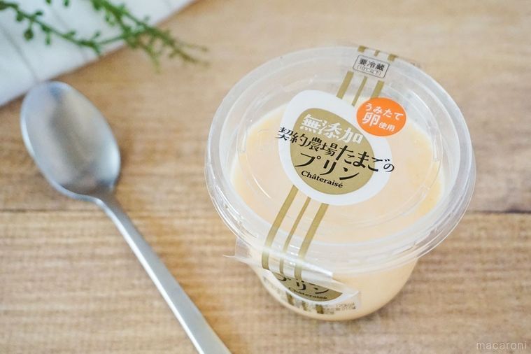 シャトレーゼ無添加 契約農場たまごのプリン銀色のスプーンと布、緑の葉を添えてテーブルに並べた様子