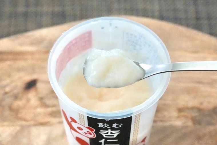 木のカッティングボードにのった飲む杏仁豆腐のドリンクカップと銀のスプーンですくう様子