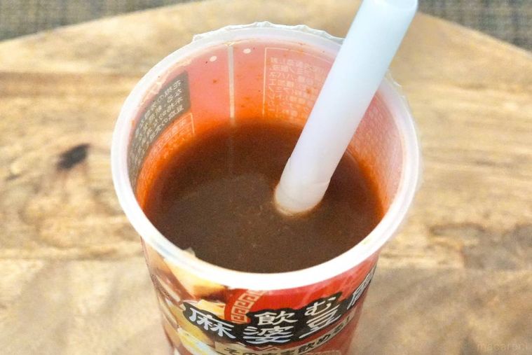 木のカッティングボードにのった赤いドリンクカップとストローと飲む麻婆豆腐