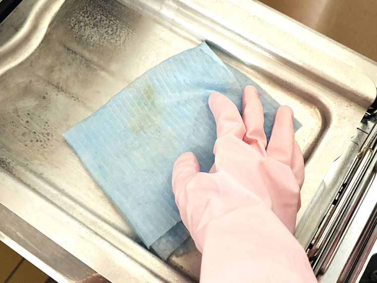 ゴム手袋を付けた手で魚焼きグリルを掃除している