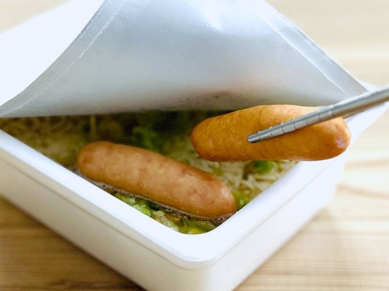 お湯が入ったカップ焼きそばにウインナーを入れている様子