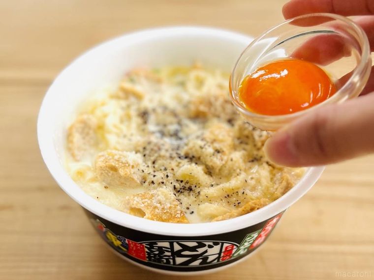 牛乳とチーズが入ったどん兵衛 きつねうどんに卵黄をのせようとしている様子