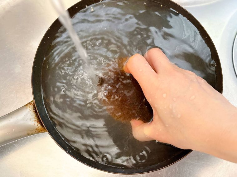 熱いフライパンに水を流しながらたわしで洗う様子