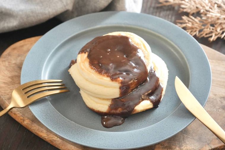 グレーの皿にのったチョコレートソースパンケーキと金色のフォークとナイフ
