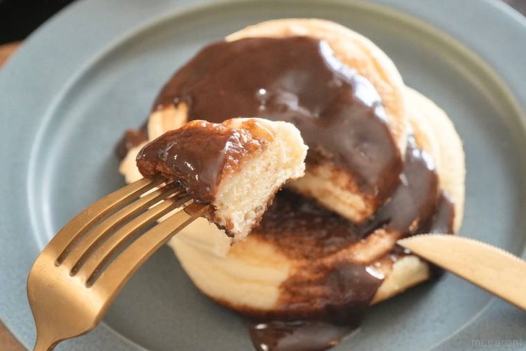 グレーの皿にのったチョコレートソースパンケーキを金色のフォークとナイフで食べる様子