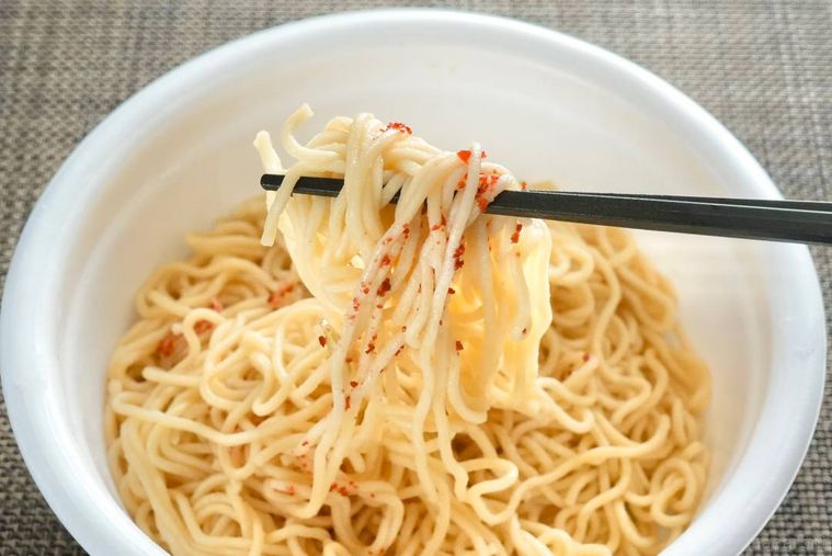 白いカップ入りの梅干し味カップ焼きそばを黒い箸で食べる様子